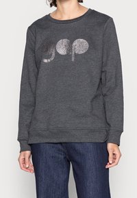 Sudadera gris oscuro con escote redondeado y mangas largas, que presenta un logo 'gap' brillante en el centro. Textura suave y corte relajado.