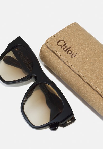 Chloé sunglasses with large black acetate frames and brown gradient lenses, accompanied by a textured beige cork case.