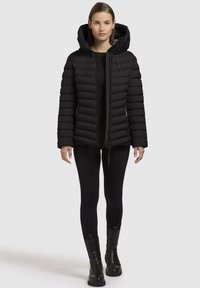 Giacca a vento nera con cappuccio, caratterizzata da un design a righe verticali, tasche con zip e lacci regolabili sull'orlo.