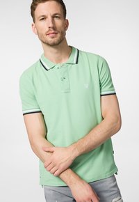 Koszulka polo z krótkim rękawem w miętowym kolorze, wykonana z bawełny, z czarno-białym kołnierzykiem w paski i trzema guzikami; logo haftowane na piersi.