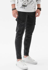 Pantalones cargo de denim negro con corte ajustado, bolsillos laterales y cremalleras. Combinados con zapatillas blancas con acentos en color menta.