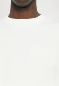 White cotton t-shirt featuring a textured, embroidered "MK" logo on the left chest area, with a classic crew neckline.