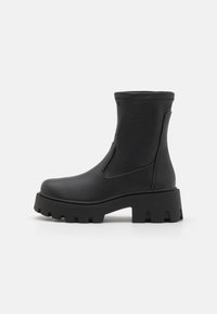 Bottines noires fabriquées en matériau synthétique lisse, dotées d'une semelle épaisse avec des crampons profonds et d'inserts élastiques sur les côtés pour un enfilage facile.