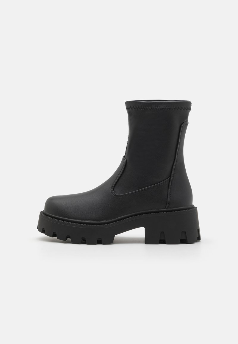 Bottines noires fabriquées en matériau synthétique lisse, dotées d'une semelle épaisse avec des crampons profonds et d'inserts élastiques sur les côtés pour un enfilage facile.