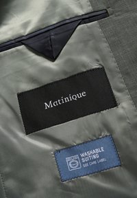 Čierna textilná etiketa nesie nápis "Matinique" na hladkej svetlosivej vnútornej podšívke. Modrá etiketa uvádza "WASHABLE SUITING" s pokynmi na starostlivosť.