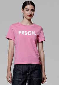 Rosa Baumwoll-T-Shirt mit kurzen Ärmeln. Mit auffälliger weißer Aufschrift "FESCH." auf der Vorderseite. Gerader Schnitt und weicher Stoff.