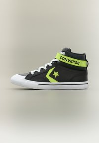 Μαύρο και νέον πράσινο αθλητικό παπούτσι Converse υψηλής κορυφής με λευκά κορδόνια και σόλα, που διαθέτει λογότυπο αστεριού και λουράκι με βέλκρο σε ουδέτερο φόντο.