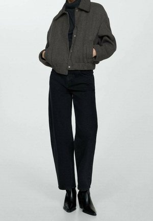 Person wearing a dark gray cropped jacket, black turtleneck, black high-waisted pants, and black heeled ankle boots on a plain background.