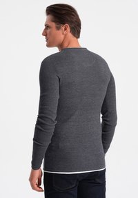 Graues Langarmshirt mit einem strukturierten Strickmuster. Verfügt über einen Rundhalsausschnitt und eng anliegende Ärmel, kombiniert mit dunklen Jeans.