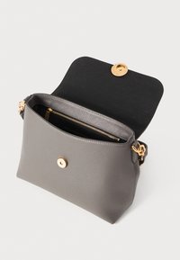 Sac à main en cuir gris avec une texture lisse, présentant une fermeture à pression circulaire dorée et une poche zippée à l'intérieur. Bandoulière ajustable incluse.