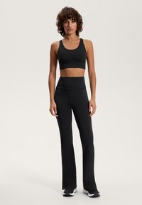 Črna športna nedrčka in visoko pasne hlače iz raztegljive tkanine z gladko teksturo; hlače imajo dizajn s širokimi nogavicami.