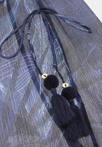 Vêtement bleu marine en tissu texturé avec des motifs de feuilles, maintenu par un lien, orné de franges noires et d'accents dorés.