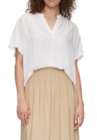Blouse blanche à manches courtes avec un décolleté en V, coupe ample, en tissu léger. Associée à une jupe beige taille haute.