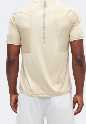 Homme portant un t-shirt de sport beige à manches courtes avec une bande réfléchissante dans le dos et un short en mesh blanc, vu de dos.