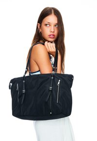 Black nylon tote bag featuring multiple exterior zippered pockets, smooth texture, and long shoulder straps. Silver hardware accents included.