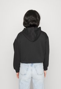 Felpa nera tagliata con finitura texturizzata e cappuccio, con strisce bianche sui lati. Abbinata a jeans strappati di colore blu chiaro.