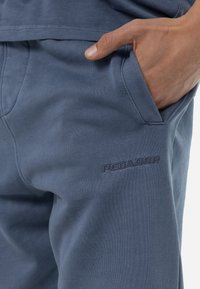 Pantalones de chándal de algodón azul con un acabado texturizado, que cuentan con bolsillos laterales y un bordado de la marca "PEGADOR" en el muslo.