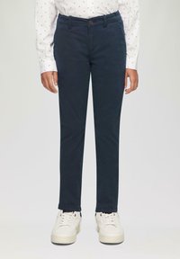 Marineblauwe chinos met een slim fit, gemaakt van katoen. Voorzien van een knoopsluiting en een subtiele glans. Gepaard met witte sneakers.
