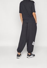 Completo sportivo nero composto da una maglietta a maniche corte e pantaloni larghi con polsini elasticizzati, impreziosito da tre strisce bianche sui lati.