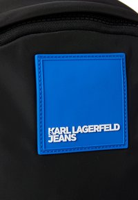 Zaino in nylon nero con un luminoso patch rettangolare blu caratterizzato da testo in rilievo bianco "KARL LAGERFELD JEANS" e cuciture a contrasto.