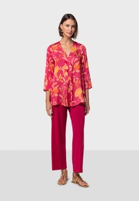 Blusa rosa de estampado floral con mangas tres cuartos y escote en V, combinada con pantalones de pierna ancha rosa sólido y sandalias doradas.