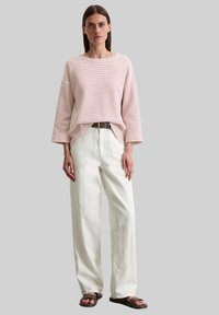 Gestreiftes, leichtes Oberteil in Pink und Weiß, lockerer Schnitt, kombiniert mit hochgeschnittenen, cremefarbenen weiten Hosen. Ein brauner Gürtel und dunkle Sandalen runden den Look ab.