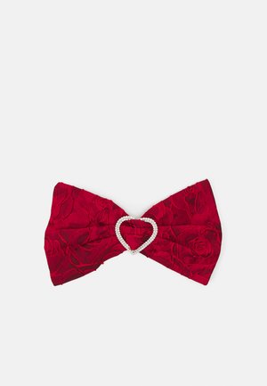 Crvena tkanina za kosu u obliku mašne, s teksturiranim cvjetnim uzorkom i akcentom u obliku srca od rhinestones na sredini.