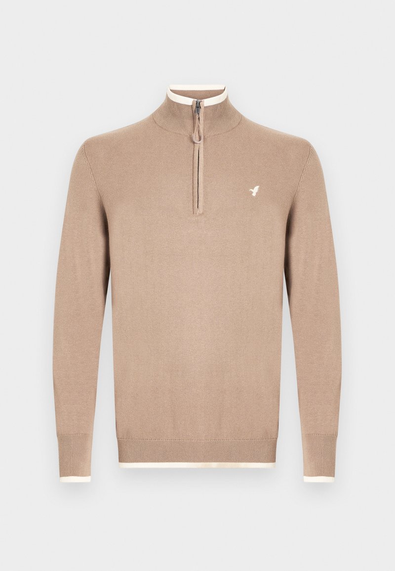 Jersey beige de punto con cuello alto y cierre de media cremallera. Presenta ribetes de color crema en el cuello y los puños, con un pequeño logo en el pecho.