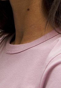 Světle růžové bavlněné tričko s kulatým výstřihem a viditelným žebrovaným límcem. Tkanina vypadá měkce s jemnou strukturou.