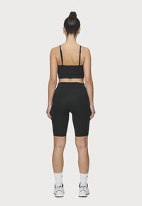 Top corto deportivo negro y pantalones cortos de ciclista de cintura alta, diseño ajustado, textura suave, llevados con calcetines blancos y zapatillas negras.