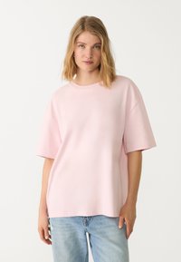 Roze oversized katoenen T-shirt met een ronde halslijn en korte mouwen, gecombineerd met lichtblauwe jeans. Eenvoudig ontwerp, zachte textuur.