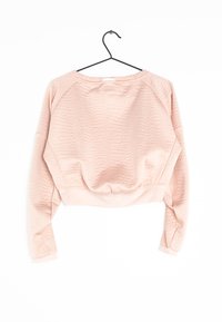 Sweatshirt cropped rose avec un tissu texturé, des manches raglan et un ourlet côtelé. Suspendu à un crochet noir pour l'exposition.