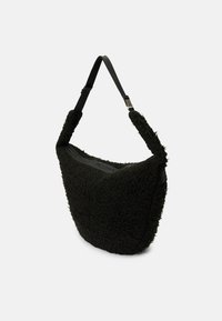 Sac noir à épaule en tissu molletonné et texturé. Il présente un design large et courbé, ainsi qu'une sangle amovible avec une fermeture éclair sécurisée.