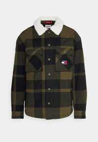 Rutigt jacka i olivgrön och svart, med en vit, konstgjord fårskinnskrage, två bröstfickor och en liten logotyp på vänster ficka.