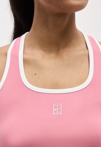 Κλείσιμο πλάνου ενός ατόμου που φορά ροζ ριπ αμάνικο τοπ με λευκή επένδυση και λευκό λογότυπο Nike στο κέντρο του στήθους.