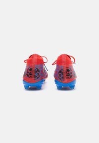 Scarpe da calcio rosse con una tomaia testurizzata, caratterizzate da accenti blu e modelli grafici neri. Tacchetti trasparenti in plastica sulla suola per una migliore aderenza.