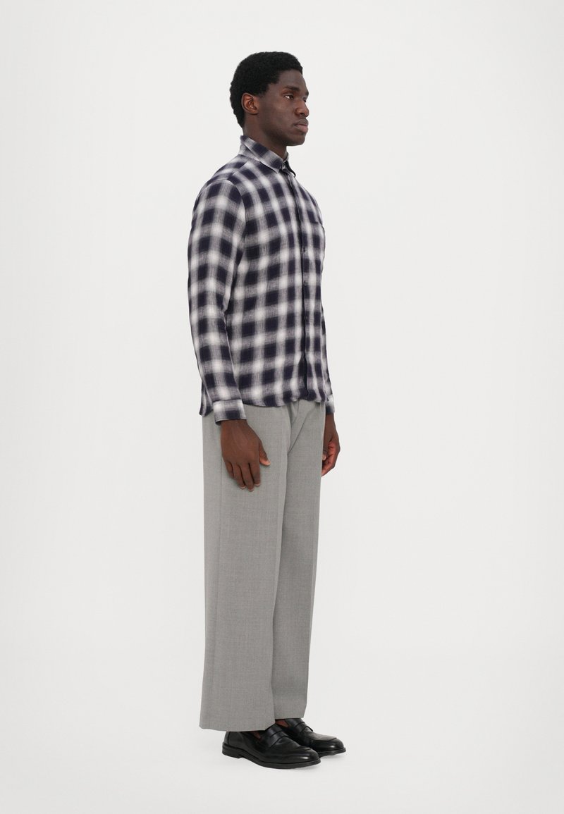 Blauw-wit geruit overhemd met knopen, gecombineerd met lichtgrijze wijde broek en zwarte schoenen. Bevat een klassieke kraag en knopen aan de voorkant.