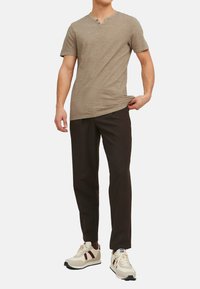 Lysbrun kortærmet V-hals T-shirt parret med mørkebrune bukser og hvide sneakers med røde og marineblå detaljer.