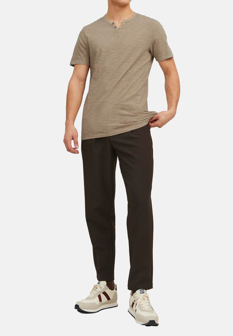 Lysbrun kortærmet V-hals T-shirt parret med mørkebrune bukser og hvide sneakers med røde og marineblå detaljer.
