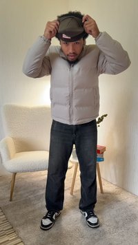 Világosszürke steppelt dzseki cipzáras rögzítéssel, texturált anyagból, oldalzsebekkel. Sötét farmernadrág és fekete-fehér sportcipők egészítik ki az öltözéket.