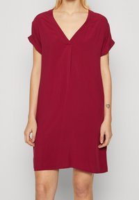 Robe à col en V et manches courtes de couleur bordeaux foncé. Tissu doux avec une coupe ample et un détail plissé à l'avant. Longueur mi-cuisse.