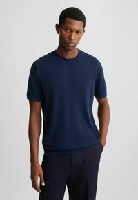 Mørkeblå t-shirt med korte ærmer i blødt stof, rund hals, afslappet pasform, med kant der slår an ved taljen. Bæret sammen med mørke bukser.