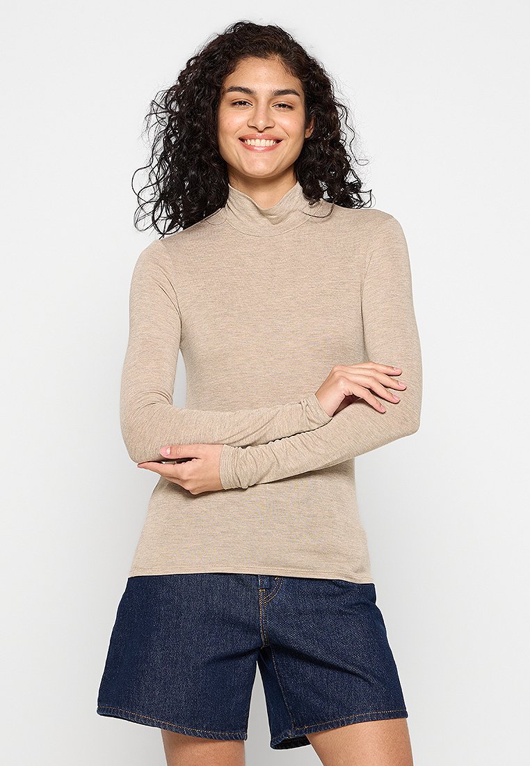Beige Langarm-Turtleneck-Shirt aus weichem, dehnbarem Stoff, kombiniert mit dunkelblauen Jeansshorts mit sichtbaren Nähten und Taschen.