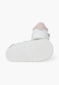 Baskets blanches avec des accents roses, tige en synthétique lisse, semelle texturée, bandes auto-agrippantes et détails en dentelle au niveau du talon.