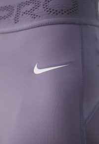 Dopasowane spodnie sportowe Nike w lawendowym kolorze z teksturowanym pasem w talii oraz białym logo swoosh na górnej części uda. Widoczne szwy.