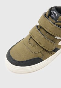 Zielone zamszowe trampki typu high-top z czarnymi akcentami, z podwójnymi paskami na rzepy, perforacjami po bokach oraz białą gumową podeszwą.
