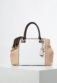 Sac à main structuré blanc et beige avec poignées noires, quincaillerie en argent et un charme ; présente une finition texturée et un détail de logo.