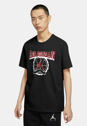 Joven con camiseta negra Air Jordan con logo rojo y blanco, combinada con pantalones cortos negros con logo blanco de Air Jordan.