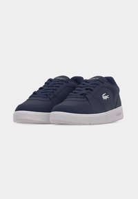Paire de baskets Lacoste bleu marine avec semelles, lacets et logo blancs sur le côté, placées côte à côte sur un fond blanc uni.