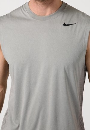 Man draagt een mouwloos lichtgrijs Nike sportshirt met een zwart swoosh-logo op de rechterborst.